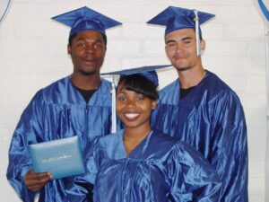 Three Corpsmembers pose with high school diplomas in cap and gowns