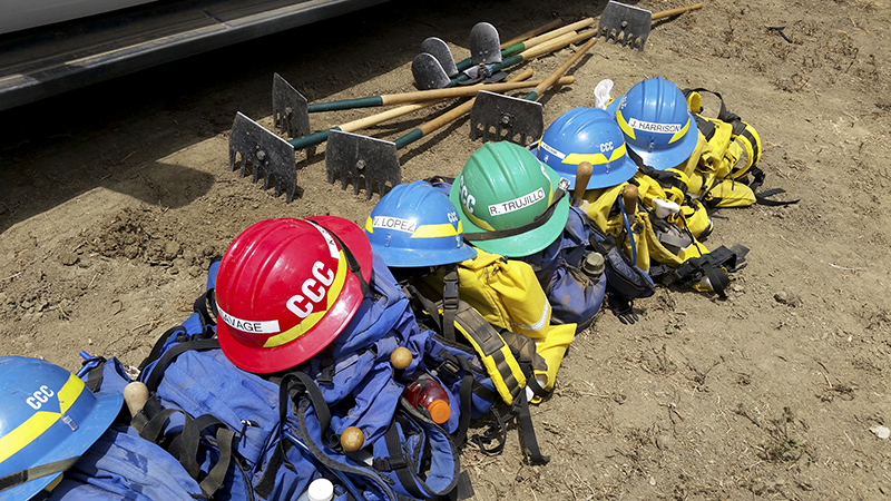 Corpsmembers with the Placer 1 fire crew cut fire line with hand tools as flames from the Dixie Fire approach in 2021.