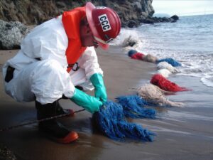 Corpsmember ties knot in tyvek suit assisting in oil spill recovery along beach