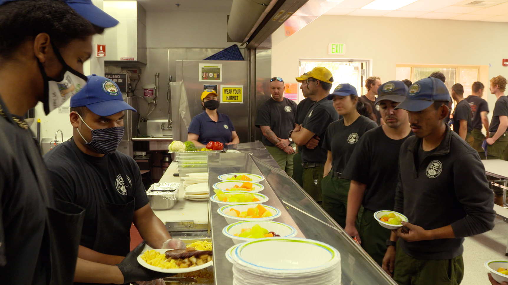 culinary corpsmembers make plates of food as firefighters tand in line