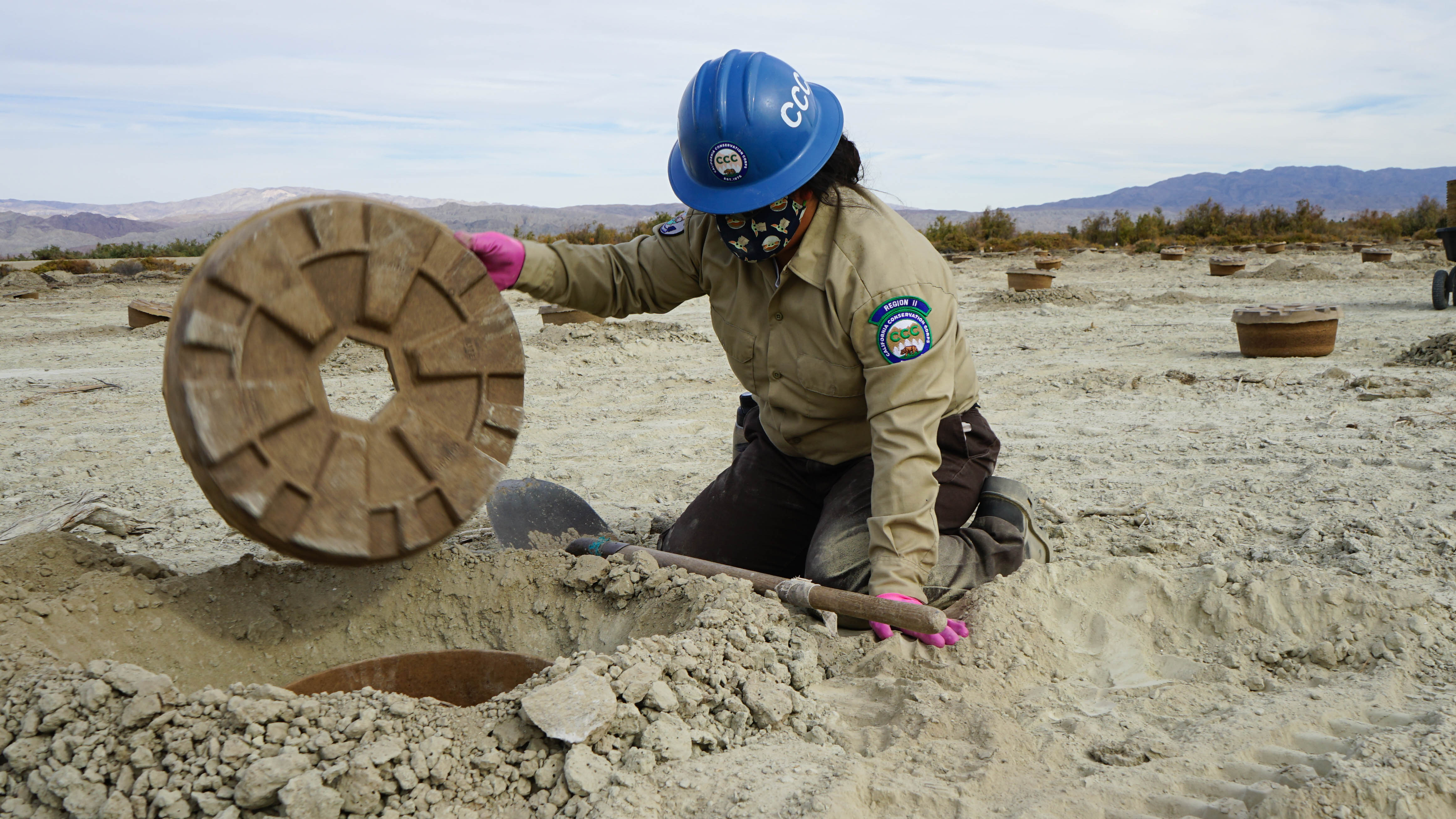 female corpsmember holding lid to cocoon above hole