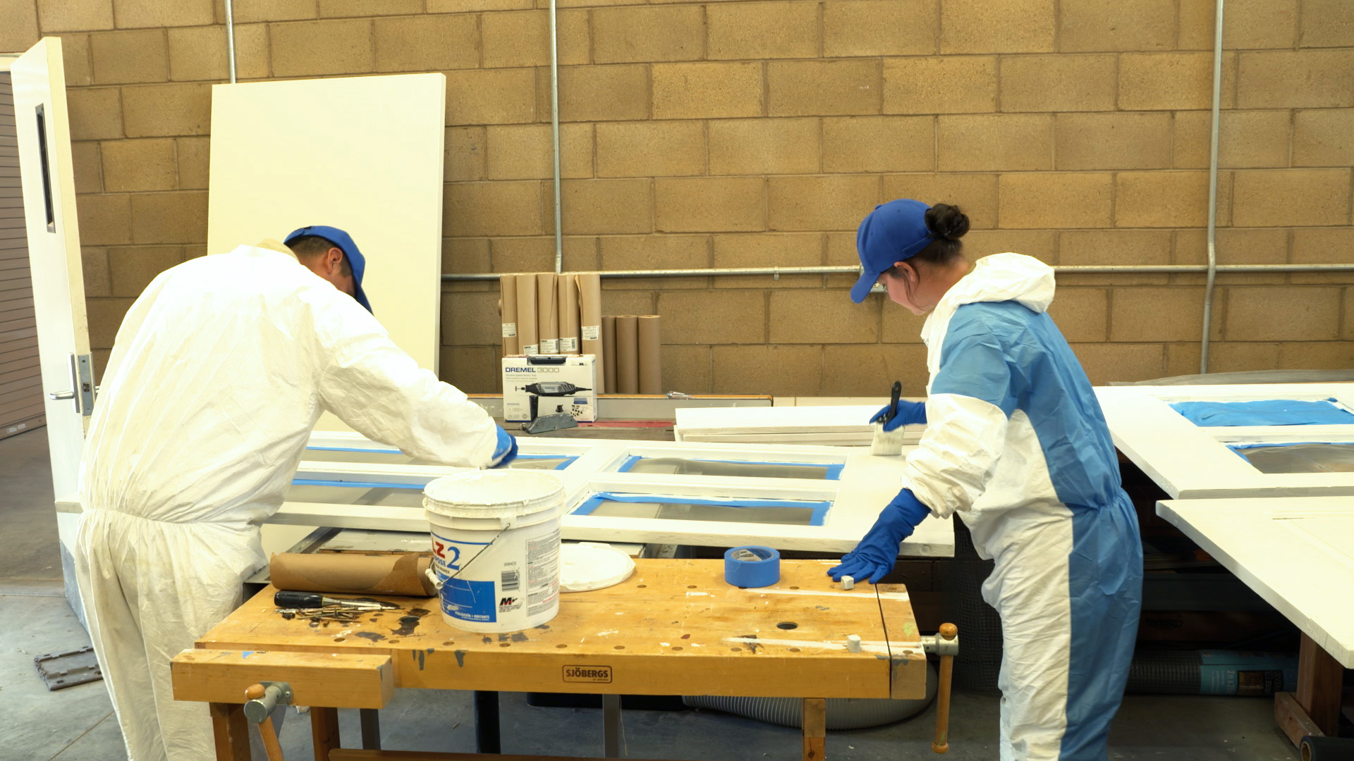 Two Corpsmembers apply white paint to a screen door. 