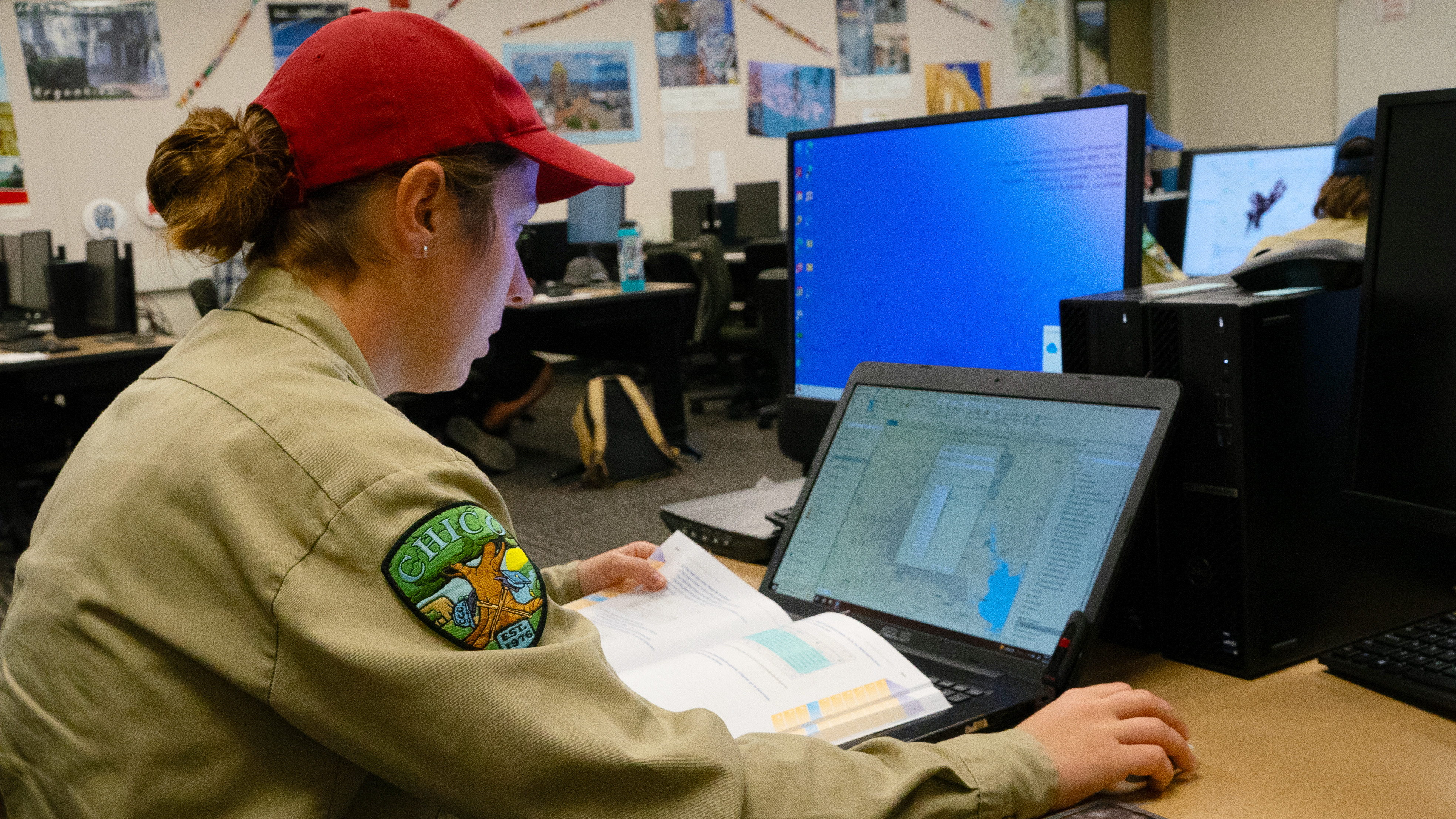 female at laptop using book to review material