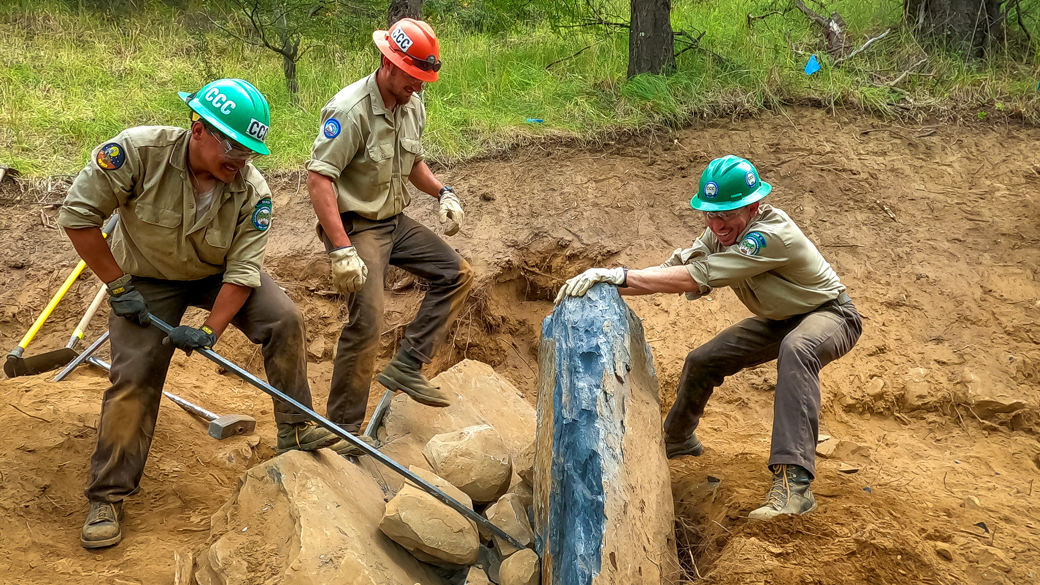 Corpsmembers use a rock bar to move a giant boulder off the trail. 