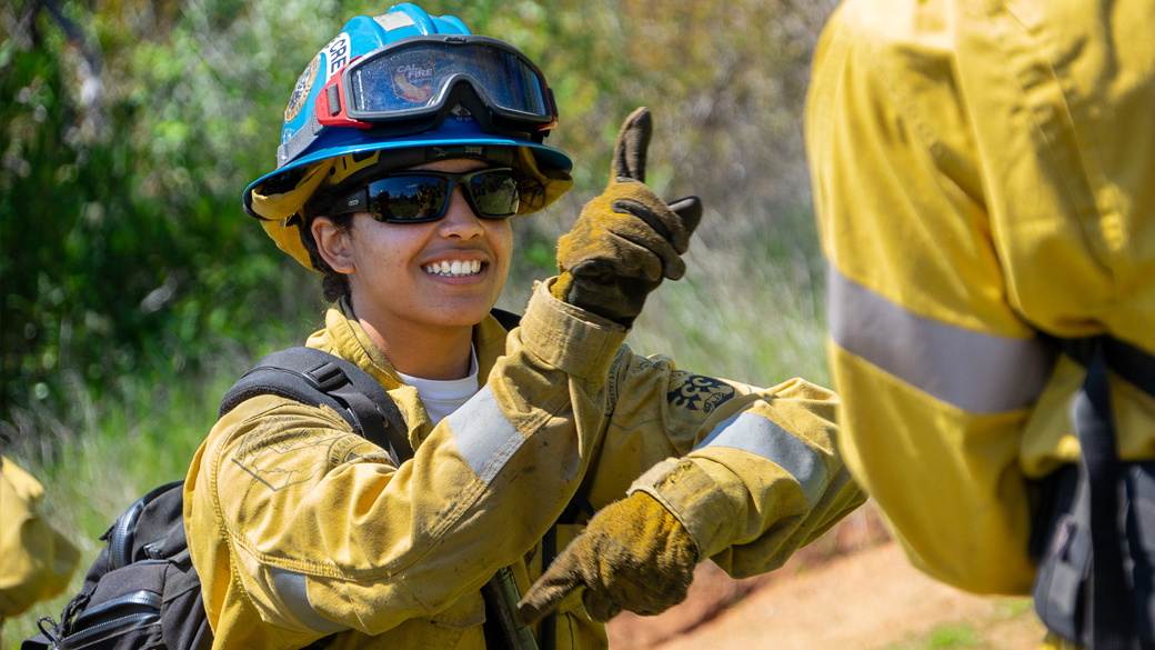 female smiling while giving a practice hand signal in fire gear