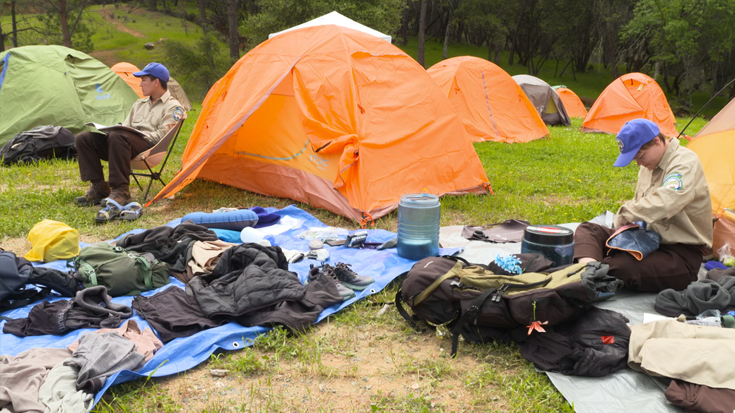 orange tents with corpsmember sitting around sifting through gear and bags