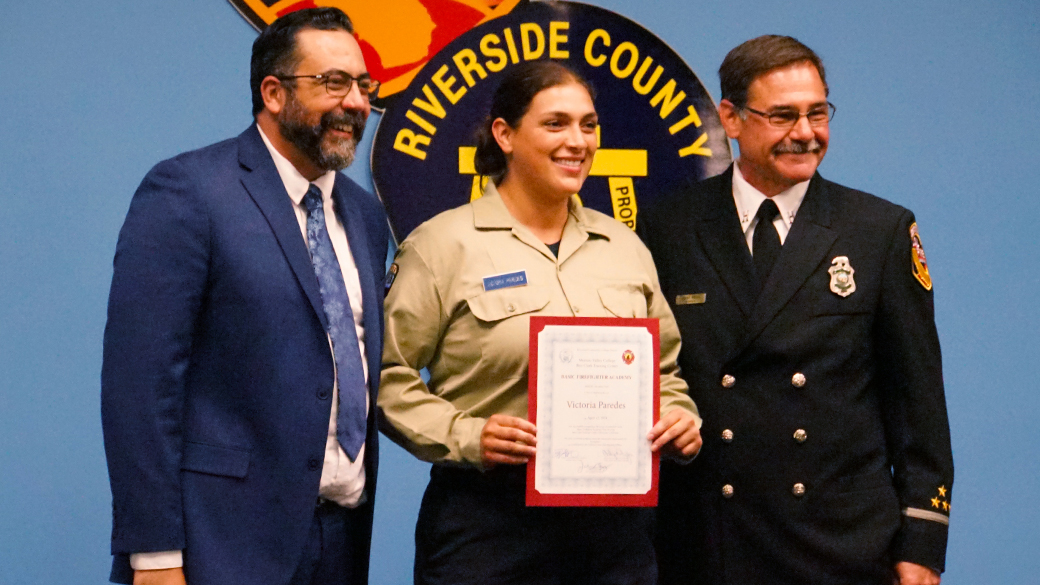 female holding graduation certificate with two men standing on either side