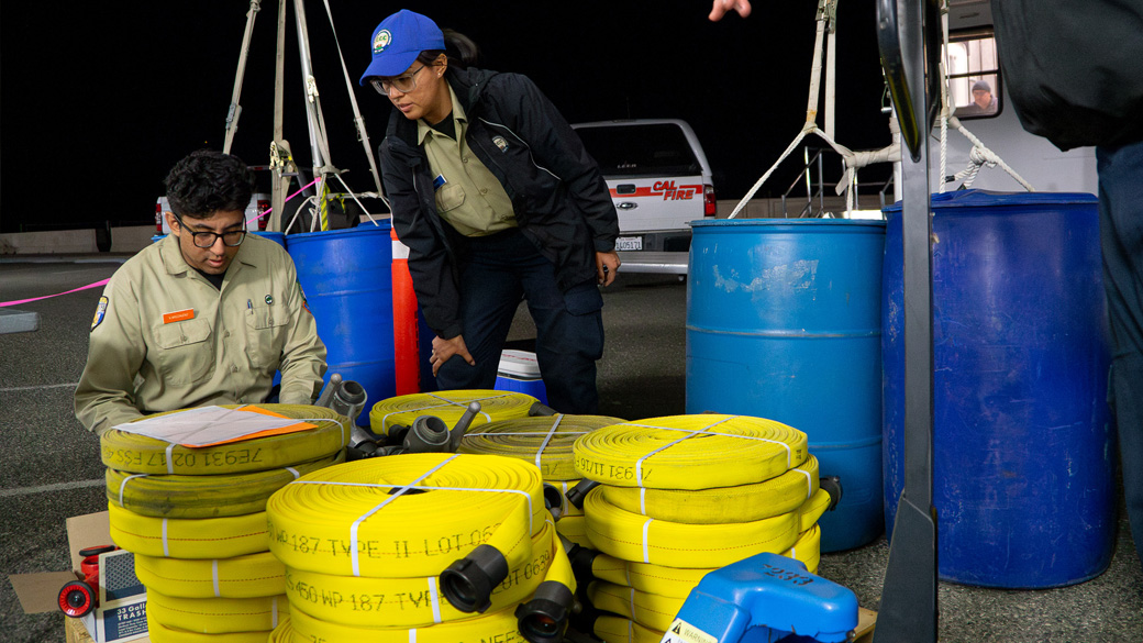 two corpsmembers reading over paperwork behind a stack of yellow fire hose