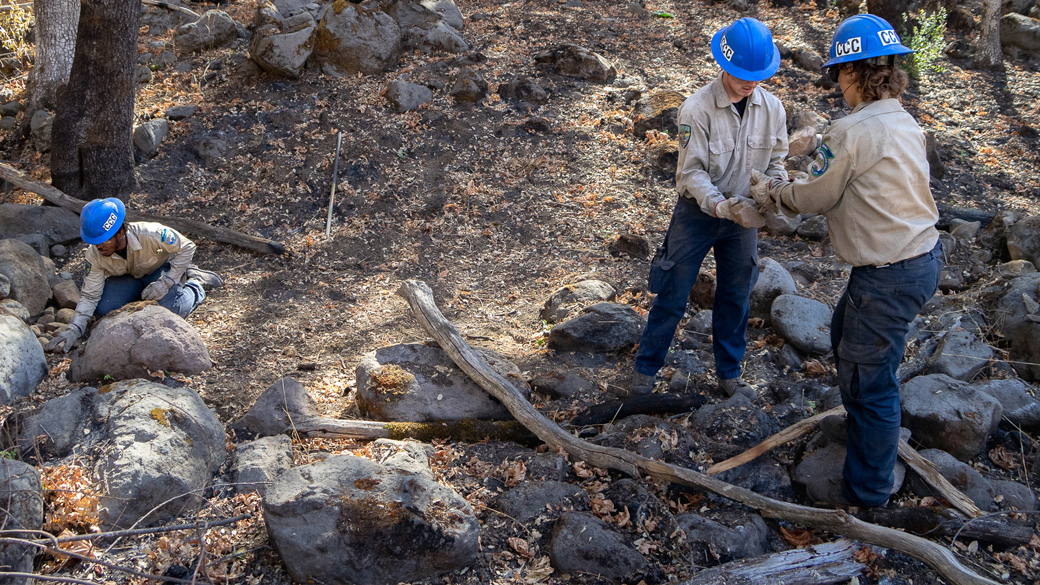 Three Corpsmembers moving rocks around a burned landscape